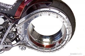 Одним из первых энтузиастов, не только размышлявших над идеей создания такого колеса, но и воплотивших ее в действующем изделии, стал Доминик Мотта. Во второй половине 80-х годов прошлого столетия этот предприниматель-авантюрист вложил часть своих сбережений в разработку новых технологий в транспорте. Работа над спорткаром будущего привела Мотта к созданию «пустого» колеса (hubless wheel, орбитальное колесо, осмос-колесо), в котором отсутствовали ступица и спицы, которое было запатентовано в 1990 году.
Несмотря на ряд преимуществ, концепция имела и существенные недостатки, главные из которых – технологическая сложность и высокая стоимость, не позволяющая использовать такое колесо в массовом производстве мотоциклов и других транспортных средств.
По сути, орбитальное колесо представляет собой чрезвычайно большой подшипник с тонкими обоймами. Внутренняя обойма – неподвижна, жестко скрепляется с рамой или с элементами подвески, наружная – вращается, на нее надевается шина и крепится тормозной диск. Приводить осмос-колесо традиционным способом непросто, в связи с этим применяется способ передачи крутящего момента с помощью фрикционного ролика, воздействующего непосредственно на поверхность шины мотоцикла. Традиционные ремни и цепи также можно использовать, но для этого на наружной обойме подшипника придется разместить, кроме всего прочего, также огромную звезду или шкив. В последнем случае, учитывая существенное увеличение ведомой звезды (по сравнению с традиционной), не лишним будет изменить передаточное отношение в трансмиссии.
Существенные изменения в конструкции переднего беcступичного колеса мотоцикла не требуются: телескопическая вилка может крепиться прямо к нижней части внутренней обоймы. Такая схема обеспечивает оптимальное распределение нагрузки на подшипник. Несмотря на преимущества связки «телескопическая вилка/орбитальное колесо», разработчики редко используют ее в своих концептах – слишком банален «телескоп» для футуристичной и революционной концепции «пустого колеса». Вместо нее используют рычажные подвески, или даже регулируемые системы, позволяющие активным смещением точки крепления обоймы к элементам подвески изменять вылет переднего колеса и, соответственно, влиять на управляемость/стабильность мотоцикла.
Известными всему миру орбитальные колеса стали несколько лет спустя после получения патента. Живая икона мирового автомобильного стиля итальянец Франко Сбарро подготовил и представил на стендах Женевского автосалона три концепта мотоциклов с бесступичными колесами, а также макеты автомобилей, среди которых была и вариация на тему «Формула-1».
Экспонаты, мягко говоря, понравились и посетителям, и журналистам. На волне высокого интереса Сбарро, Мотта, а также компании Pirelli и SRO-FAG основали компанию по производству осмос-колес. Основатели пророчили новой концепции широкое распространение не только на асфальте, но и на железной дороге и даже в космосе. Покупатели не спешили расставаться со своими деньгами, ведь в виду сложности конструкции стоимость колес оказалась неподъемной для производителей массовых моделей мотоциклов и автомобилей.
Концепцию колеса Сбарро забыл, после того, как использовал ее для создания новой марки оригинальных часов, доступных покупателям по цене от 3500 Евро. Доминик Мотта не смог так просто расстаться со своим детищем и продолжил поиск инвесторов по всему миру. Он предлагал использовать концепцию производителям мотоциклов (Yamaha, Echelon), автомобилей (Ferrari, BMW, Daimler, Nissan, General Motors, Ford, VW, Volvo), поездов (Alstom), велосипедов (Cycleurope, Shimano). Главным барьером на запуске бесступичных колес в массовое производство и, соответственно, их удешевлении стал владелец патентов – швейцарская компания Globeholding.
Таким образом, идею орбитального колеса в течение многих лет использовали исключительно энтузиасты, собирающие уникальные байки в своих гаражах. Но в 2008 году на мотовыставке в немецком Кельне компания Honda представила свое видение мотоцикла будущего под названием Honda V4 Concept, колеса которого имели орбитальную конструкцию. Представленный байк не имел привычного современному мотоциклисту приводного ремня, цепи или карданного вала, а функция передачи крутящего момента на колесо была поручена валику, воздействующему непосредственно на шину. Но самым интересным оказался даже не сам концепт, а заверение производителя запустить его в массовое производство уже в 2010 году. В результате Honda V4 Concept остался всего лишь красивой картинкой и ярким воспоминанием для посетителей мотосалона.
Одним из самых известных байков современности с осмос-колесами, который можно увидеть не только в интернете, но и на улицах, является творение компании Amen Design and Engineering. Чоппер с передним и задним «пустыми» колесами выглядит в высшей степени оригинально и, что самое главное, полностью функционален. Он уверенно ездит по дорогам общего пользования.
Создатели и поклонники необычного байка в список достоинств безспицевых колес записывают их малый вес, уменьшенные вибрации, улучшенные характеристики торможения. При этом никто не отрицает их дороговизны и сложности в производстве. Вращение колес обеспечивают 850 подшипниковых шариков, на дорогу байк опирается 120-миллиметровой (ширина) передней и 360-миллиметровой задней шинами.