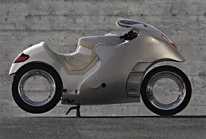 Одним из первых энтузиастов, не только размышлявших над идеей создания такого колеса, но и воплотивших ее в действующем изделии, стал Доминик Мотта. Во второй половине 80-х годов прошлого столетия этот предприниматель-авантюрист вложил часть своих сбережений в разработку новых технологий в транспорте. Работа над спорткаром будущего привела Мотта к созданию «пустого» колеса (hubless wheel, орбитальное колесо, осмос-колесо), в котором отсутствовали ступица и спицы, которое было запатентовано в 1990 году.
Несмотря на ряд преимуществ, концепция имела и существенные недостатки, главные из которых – технологическая сложность и высокая стоимость, не позволяющая использовать такое колесо в массовом производстве мотоциклов и других транспортных средств.
По сути, орбитальное колесо представляет собой чрезвычайно большой подшипник с тонкими обоймами. Внутренняя обойма – неподвижна, жестко скрепляется с рамой или с элементами подвески, наружная – вращается, на нее надевается шина и крепится тормозной диск. Приводить осмос-колесо традиционным способом непросто, в связи с этим применяется способ передачи крутящего момента с помощью фрикционного ролика, воздействующего непосредственно на поверхность шины мотоцикла. Традиционные ремни и цепи также можно использовать, но для этого на наружной обойме подшипника придется разместить, кроме всего прочего, также огромную звезду или шкив. В последнем случае, учитывая существенное увеличение ведомой звезды (по сравнению с традиционной), не лишним будет изменить передаточное отношение в трансмиссии.
Существенные изменения в конструкции переднего беcступичного колеса мотоцикла не требуются: телескопическая вилка может крепиться прямо к нижней части внутренней обоймы. Такая схема обеспечивает оптимальное распределение нагрузки на подшипник. Несмотря на преимущества связки «телескопическая вилка/орбитальное колесо», разработчики редко используют ее в своих концептах – слишком банален «телескоп» для футуристичной и революционной концепции «пустого колеса». Вместо нее используют рычажные подвески, или даже регулируемые системы, позволяющие активным смещением точки крепления обоймы к элементам подвески изменять вылет переднего колеса и, соответственно, влиять на управляемость/стабильность мотоцикла.
Известными всему миру орбитальные колеса стали несколько лет спустя после получения патента. Живая икона мирового автомобильного стиля итальянец Франко Сбарро подготовил и представил на стендах Женевского автосалона три концепта мотоциклов с бесступичными колесами, а также макеты автомобилей, среди которых была и вариация на тему «Формула-1».
Экспонаты, мягко говоря, понравились и посетителям, и журналистам. На волне высокого интереса Сбарро, Мотта, а также компании Pirelli и SRO-FAG основали компанию по производству осмос-колес. Основатели пророчили новой концепции широкое распространение не только на асфальте, но и на железной дороге и даже в космосе. Покупатели не спешили расставаться со своими деньгами, ведь в виду сложности конструкции стоимость колес оказалась неподъемной для производителей массовых моделей мотоциклов и автомобилей.
Концепцию колеса Сбарро забыл, после того, как использовал ее для создания новой марки оригинальных часов, доступных покупателям по цене от 3500 Евро. Доминик Мотта не смог так просто расстаться со своим детищем и продолжил поиск инвесторов по всему миру. Он предлагал использовать концепцию производителям мотоциклов (Yamaha, Echelon), автомобилей (Ferrari, BMW, Daimler, Nissan, General Motors, Ford, VW, Volvo), поездов (Alstom), велосипедов (Cycleurope, Shimano). Главным барьером на запуске бесступичных колес в массовое производство и, соответственно, их удешевлении стал владелец патентов – швейцарская компания Globeholding.
Таким образом, идею орбитального колеса в течение многих лет использовали исключительно энтузиасты, собирающие уникальные байки в своих гаражах. Но в 2008 году на мотовыставке в немецком Кельне компания Honda представила свое видение мотоцикла будущего под названием Honda V4 Concept, колеса которого имели орбитальную конструкцию. Представленный байк не имел привычного современному мотоциклисту приводного ремня, цепи или карданного вала, а функция передачи крутящего момента на колесо была поручена валику, воздействующему непосредственно на шину. Но самым интересным оказался даже не сам концепт, а заверение производителя запустить его в массовое производство уже в 2010 году. В результате Honda V4 Concept остался всего лишь красивой картинкой и ярким воспоминанием для посетителей мотосалона.
Одним из самых известных байков современности с осмос-колесами, который можно увидеть не только в интернете, но и на улицах, является творение компании Amen Design and Engineering. Чоппер с передним и задним «пустыми» колесами выглядит в высшей степени оригинально и, что самое главное, полностью функционален. Он уверенно ездит по дорогам общего пользования.
Создатели и поклонники необычного байка в список достоинств безспицевых колес записывают их малый вес, уменьшенные вибрации, улучшенные характеристики торможения. При этом никто не отрицает их дороговизны и сложности в производстве. Вращение колес обеспечивают 850 подшипниковых шариков, на дорогу байк опирается 120-миллиметровой (ширина) передней и 360-миллиметровой задней шинами.