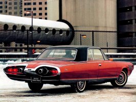 В 1963 году "Chrysler" стал первым в мире автопроизводителем, запустившим газотурбинные автомобили в серийное производство. Chrysler Corp. развернула уникальную программу под лозунгом «dream car в жизнь». Впервые в истории начался (мелко)серийный выпуск «автомобиля мечты» под говорящим названием Chrysler Turbine: легковушка с газотурбинным двигателем. Не только (и не столько) для выставок и демонстраций, сколько для повседневной эксплуатации. По замыслу, экспериментальная модель строилась в 55 экземплярах, из которых полсотни предназначались к раздаче в пользование американским автомобилистам по всей стране.
Как выбирали счастливых участников масштабного эксперимента — отдельный разговор. Так или иначе в октябре 1963 м-р Lynn A.Townsend, тогдашний президент Chrysler Corp., лично вручил ключи от новенького Chrysler Turbine первым пользователям – рядовой семье из чикагского пригорода. Процесс пошел. По программе, каждый из участников эксплуатировал машину в течение трех месяцев, а затем передавал ее очередному. Всего в эксперимент вовлекались две сотни автомобилистов. В Chrysler Corp. рассчитывали получить неоценимые сведения об эксплуатационных качествах «турбинной» легковушки – в условиях, приближенных к боевым. А также проверить реакцию потенциальных покупателей на непривычное транспортное средство – и оценить его рыночный потенциал.
Прогрессивная турбина вместо безнадежно устаревшего д.в.с. – вот ведущая идея крайслеровского dream car образца 1963. И в самом деле под капотом размещался газотурбинный двигатель (уже IV поколения) с вращающимися регенераторами тепла отработанных газов. Их температура на выхлопе падала до каких-то 245о C, — то есть, тепловая энергия утилизировалась довольно глубоко. Компактный агрегат весил 185+ кг и стыковался с 3-скоростным «автоматом» TorqueFlite (без гидротрансформатора, надобность в котором отпала в силу 2-вальной конструкции турбины).
Объявленная максимальная мощность агрегата (SAE «нетто») – 130 л.с. при 3600 оборотах выходного вала. То есть, сама-то вторичная (тяговая) турбина крутилась при максимальной мощности на 44600 мин-1, однако обороты понижались встроенным понижающим редуктором – до обычного в легковом автомобилестроении уровня («отсечка» на 4680 мин-1). Не сказать, что турбина отличалась выдающейся мощностью (тогда уже делали литражные «восьмерки» и на 400 сил – «брутто»). Зато крутящий момент она выдавала (на выходном валу) очень неслабый — за 575 Нм. Причем прямо от 0 оборотов, так что на разгонную динамику Chrysler Turbine никто не жаловался.
Мощная тяга транслировалась на неразрезный ведущий мост, подвешенный на продольных листовых рессорах. Передняя подвеска – на двойных поперечных рычагах, стандартная для американской легковушки тех лет ходовая. Узенькие (по нынешним понятиям) покрышки с диагональным кордом – и барабанные тормоза «по кругу». Рулевой механизм «винт-шариковая гайка» с гидроусилителем – все как у всех в начале 60-х. Так что Chrysler Turbine представлял собой пеструю мозаику передовых и традиционных (а где-то даже устаревших) технических решений, осторожное продвижение.
Как обычно для газовых турбин, крайслеровский агрегат оказался по-настоящему многотопливным: он успешно работал на неэтилированном бензине и авиационном керосине. И даже на растительном масле, хотя участникам эксперимента рекомендовали стандартное дизтопливо. Газотурбинный агрегат работал исключительно надежно и не доставлял добровольцам особенных хлопот.
Программа благополучно завершилась в начале 1965, после чего полсотни «турбинных» легковушек отправили на слом. В течении трех лет на этих автомобилях поездило около 200 человек, преимущественно проверенных клиентов фирмы, которые и вынесли неутешительный вердикт. Да, экзотичный мотор "Chrysler Turbine Car" превосходен по характеристикам. Он настолько тяговит и высокооборотен, что нет нужды в КПП — двигатель вращает ведущие колеса напрямую. Увы, но газовая турбина свистит как Соловей-разбойник, что невыносимо в дальних поездках. Второй недостаток — непомерный расход топлива, составлявший порядка 24 л /100 км. Чудовищный аппетит для относительно небольшой машины. В итоге программу газотурбинных автомобилей закрыли.