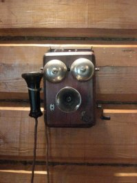 Напомнило:

"Иван Францевич остановился возле «аппарата Белла», снял рожкообразную трубку, приложил к <span style='color:gray'>[мат]</span> покрутил какой-то рычажок. Аппарат хрюкнул, в нем что-то звякнуло. Бриллинг приставил ухо к другому рожку, торчавшему из лакированного ящика, и в рожке запищало. Фандорину показалось, что он разобрал, как тоненький голосок смешно проговорил слова «дежурный адъютант» и еще «канцелярия».

— Новгородцев, вы? — заорал в трубку Бриллинг. — на месте ли его превосходительство? Нет? Не слышу! Нет-нет, не надо. Не надо, говорю! — он набрал в грудь побольше воздуха и закричал еще громче. — Срочный наряд для задержания! Немедленно отправьте на Аптекарский остров! Ап-те-кар-ский! Да! Флигель эстерната! Эс-тер-на-та! Неважно, что это значит, они разберутся! И пусть группа обыска приедет! Что? Да, буду лично. Быстрей, майор, быстрей!

Он водрузил трубку на место и вытер лоб.

— Уф. Надеюсь, мистер Белл усовершенствует конструкцию, иначе все мои соседи будут в курсе тайных операций Третьего отделения.

Эраст Петрович находился под впечатлением волшебства, только что свершившегося на его глазах."
Б.Акунин. "Азазель".