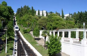 Такая ж/д называется ФУНИКУЛЁР!
Принцип действия: один конец каната опускает вагон, второй - тянет. Мотор помогает.
Зубчатых колес там не видел.
Россия, Сочи, запущен в работу 1934 году.
Длина пути не большая. 
Бесплатно.