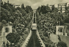 Такая ж/д называется ФУНИКУЛЁР!
Принцип действия: один конец каната опускает вагон, второй - тянет. Мотор помогает.
Зубчатых колес там не видел.
Россия, Сочи, запущен в работу 1934 году.
Длина пути не большая. 
Бесплатно.