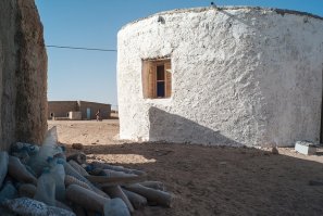 Оригинал статьи.
Немного гугл перевода:
Около 90 000 беженцев-сахрави живут в пяти лагерях неподалеку от алжирского города Тиндуф в палатках и кирпичных домах из глины, которые предлагают скудную защиту от сурового климата Сахары.
Брейка, который имеет степень магистра в области энергоэффективности, построил первый дом для своей бабушки, используя 6000 пластиковых бутылок, наполненных песком.
Он обнаружил, что, кладя заполненные песком бутылки рядом, как кирпичи, он может построить дом, который не упадет. Круглая форма защищает от движущих ветров, а стенки бутылки обеспечивают прочную, прочную конструкцию, выдерживающую дождь.
Как только основная конструкция будет построена, стены будут покрыты цементом и известняком, а затем покрашены в белый цвет, чтобы отражать солнечные лучи и поддерживать температуру в помещении.
Его дома могут быть построены всего за одну неделю по цене около 270 долларов США, что составляет четверть стоимости кирпичного дома из глины.
П.С. Так что для этих беженцев пластиковая бутылка не загаживает планету, а помогает выжить.

 Пластиковая бутылка в 20 раз прочнее, чем глинобитный кирпич , - подчеркнул юный сахарский инженер.
Татех Лебиб, инженер-сахрави
Проект Лебиба был поддержан Агентством ООН по делам беженцев (УВКБ) с бюджетом 60 000 евро. Он до сих пор построил 26 домов, в которых 80 процентов используемых материалов были переработанного пластика, соломы, земли и картона. В бутылках, которые составляют основу и структуру стен, используются либо одно-, либо двухлитровые бутылки с водой или содовой, которые можно найти в лагерях и на свалках.
 Цель состоит в том, чтобы облегчить страдания сахарцев, позволить им жить с большим достоинством и строить экологичные и устойчивые дома , - пояснил инженер.