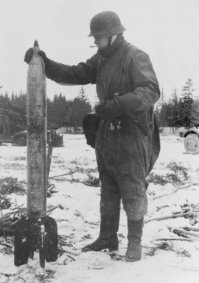 Немецкий солдат со 132-мм реактивным снарядом М-13 (ОФ-941) от советской боевой машины реактивной артиллерии БМ-13  Катюша  (на заднем плане), потерянной в районе Можайска в октябре 1941 года.