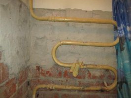 В брежневских постройках 70-х вся задняя стена ЗА санузлом и задняя стена кухни - вентканалы. Бетонные блоки, поделённые на вентпроходы примерно 15-20 см. в ширину каждый. У каждой квартиры вход в свой канал. В санузле перед вентканалом находится стенка самого санузла, она не доходит до потолка гдето 30-35 см. . где и прорублены вентотверстия. В туалете в одном из вентканалов проложен канализационный стояк. Напорные трубы там не прокладывали. то, что находится за унитазом на этом фото - не брежневка. Это больше похоже на кирпичные точки, там были такие ниши под коммуникации. Но в тех домах вентканалы похожи на современные - центральный "стояк" со входами в него из квартир. Располагался всегда между кухней и ванной (из-за габаритов).
это либо какой то спецпроект, либо капитальная перестройка дореволюционного здания.
Но в любых стандартных домах Стояки под змеевики шли либо по туалету, либо ванне и на змеевик трубы проходили только стену санблока. Это технология - трубы по санблоку монтировались на заводе, на месте подключались только межэтажные переходы. здесь же стояки напоминают сталинские здания, но там не было санблоков (они появились позже) . Но даже в сталинках вот так вот змеевики  не подлючали - очень сложно монтировать и обслуживать. 

Внизу - стандартный полотенцесушитель СССР со стандартным подключением