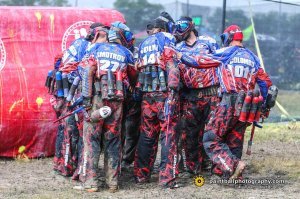 А давайте посмотрим, что здесь пытались сравнить!
1.1. Спецназ. 
В тяжелых брониках, касках, противоосколочных очках, но чаще - с открытыми глазами, в наколенниках и иногда - налокотниках, которые при скольжении по поверхности сползают.
Вооружение: автоматы Калашникова, в том числе с подствольными гранатометами (в случае необходимости), пистолеты, свето-шумовые и боевые гранаты. В составе группы могут быть пулеметчики, снайперы. 
Оружие точное, количество патронов в магазине небольшое, при выстреле происходит отдача. 
Дополнительный боезапас носится спереди, заряжание производится с нижней части оружия.
Оружие стреляет точно на достаточно больших для пейнтбола дистанциях, как правило работа ведется точными одиночными выстрелами или короткими очередями. Небольшой кустарник не является помехой для поражения.
В случае поражения противником, боец получает реальные травмы или погибает, соответственно, тактика боя строится в том числе исходя из этого.
1.2. Профессиональный спортивный пейнтбол
У каждого личный пристрелянный автоматический маркер, стреляющий очередями при нажатии на мягкий спуск, с кевларовым балоном, электронным фидером, автоматически с большой скоростью подающим шары, с крышкой, позволяющей засыпать шары, не открывая фидер, харнес с тубами, носимый за спиной, личная маска, с хорошими стеклами, пейнтбольная форма с усиленной защитой ног, паха, локтей, что позволяет делать подкаты с разбега.
Точность маркеров относительно небольшая, так как шары не идеально сбалансированы, на больших дальностях необходимо делать поправки, шары разлетаются при попадании в кустарник, не всегда пролетая насквозь.
Вместимость фидера около 200 шаров, засыпание шаров производится сверху маркера. 
Оружие нелетальное.
Всё это позволяет вести работу большими очередями, не бояться делать "прорывы", так как пораженный боец не получает никаких травм (только если сам неудачно упадёт).

2. С чем вышли на поле.
2.1.Спецназ
Дешевые прокатные маркеры, делающие один выстрел при одном нажатии на тугой спусковой крючок, с дешевыми фидерами, подающими шары за счет их собственного веса, из-за чего бывают холостые выстрелы при высокой интенсивности стрельбы, пологом наклоне маркера или когда три шара упираются друг в друга, перекрыв"воронку", с алюминиевым балоном. 
Шары размещены в прокатных харнессах с размещением туб за спиной. Засыпание производится сверху после открывания крышки фидера, после чего её нужно закрыть.
Маски тоже дешевые прокатные, запотевающие после легкой пробежки. Форма обычная с привычными для спецназа наколенниками.
Прокатные стволы маркеров могут быть грязные, царапанные, т.е. точность стрельбы тоже под сомнением.
2.2. Пейнтболисты
Всё своё.

Когда я это увидел, то просто пролистал в конец ролика, чтобы убедиться в правоте своих предположений о результате встречи.
Считаю, что более честным было бы провести встречу пейнтболистов и спецназа с использованием ОДИНАКОВОГО страйкбольного снаряжения или хотя бы дешевого прокатного пейнтбольного.
ПС. Автомат в руках держал, маркер тоже.