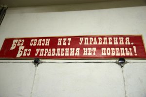 Фото от туда же. Сдается мне это не для партийных товарищей строили. Это был ЗКП (запасной командный пункт) Прибалтийского округа либо штаб Гражданской обороны, либо же пункт управления Округа.
На военный характер объекта намекает характерное расположение столов дежурных, плакаты.
Остальное видимо натащили из гражданских объектов уже позже ( плакаты ГО, противогазы и знамена).