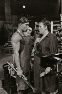 Сильно смахивает на постанову - 1) нафига работяге такой здоровый рожковый ключ? В легковых машинах гаек такого размера для рожкового ключа просто нет, а в грузовых гайки таким ключом слижутся "на раз", для таких неподатливых гаек используются головки или накидные ключи, а для податливых такое удлинение трубой просто не нужно. 2) Нафига гаечный ключ в руку руководителя? Неужели руководитель объясняет работяге, как правильно крутить гайки? :) 3) нафига при разговоре с кем бы то ни было рабочему держать в руках аж две неудобные и увесистые железяки? Почему бы их не оставить рядом с рабочим местом? 4) фартук вроде бы запачкан, а верхняя тесемка белая и чистая. Работяга что, стирает её каждый раз после снятия фартука? 5) могу ошибаться, но для рабочих куртка-роба вроде обязательна. Да и вообще этот "работяга" какой-то чересчур чистый и гладкий для работяги сборочного цеха, такое ощущение, что нашли какого-то спортсмена, надели ему новый фартук, слегка его испачкали, сказали, подержи в руках для антуража вот эти не сочетающиеся друг с другом железки, а мы сфотографируем тебя для репортажа "тетка из парткома учит работягу крутить гайки", для усиления роли "руководящей и направляющей" :)