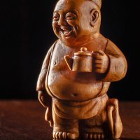 Миниатюрная скульптура «Чайханщик» 
Дерево, высота 5,8 см.  Символ гостеприимства, добродушия и открытости.
Чайханщик - мужчина средних лет добродушный, смешливый толстяк, умеющий поднять настроение и развеселить. Знает много весёлых анекдотов и поучительных историй. Знает все последние новости. В любое время рад новым людям и гостям. Когда бы вы ни посетили его, он встретит вас весёлым настроением и жизнеутверждающим оптимизмом. Он всегда готов накормить вкусной пищей и угостить душистым чаем. В его чайхане всегда спокойно и уютно. Его общение с вами начинается с омовения ваших рук и лица. Как гостеприимный хозяин он сам польёт вам на руки из кумгана, при этом пожелает вам и вашим детям земных благ, покоя и процветания. Полив вам из кумгана, он подаст вам полотенце расшитое растительным орнаментом руками его жены. Полотенце символизирует землю, которая впитывает воду. После того как вы усядетесь за дастарханом, вам подадут чай в небольшом чайничке и пиалы. Чай утолит жажду, взбодрит и настроит на благостное расположение духа. Когда вы будете пить терпкий чай и в знак уважения и признательности пригласите хозяина к своему столу, он расскажет вам все новости дня, рассмешит вас, и вы не заметите, как подадут вам ароматный плов. Если вы хоть раз бывали в чайхане у чайханщика, то вам всегда будет приятно побывать здесь ещё раз.