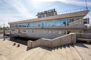 Тоже весьма необычная судьба у дебаркадера.
Поставлен у Ждановской набережной в Ленинграде в конце 1960х. Внутри был бар на первом этаже, и ресторан "Парус" на втором.
Под конец 90х был переделан в плавучий корпус частного ВУЗа, на нем размещалась библиотека и лаборатории. В 2012 у дебаркадера появился новы владелец, и внезапно началось интересное. Оказалось, что построенный в СССР и простоявший 30 лет по этому адресу дебаркадер стоит там незаконно. Пока шли разбирательства дебаркадер потонул. В итоге в 2013 его подняли, и отбуксировали на другое место стоянки. Но  пару лет назад он вернулся обратно, теперь там гостиница.