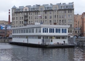 Тоже весьма необычная судьба у дебаркадера.
Поставлен у Ждановской набережной в Ленинграде в конце 1960х. Внутри был бар на первом этаже, и ресторан "Парус" на втором.
Под конец 90х был переделан в плавучий корпус частного ВУЗа, на нем размещалась библиотека и лаборатории. В 2012 у дебаркадера появился новы владелец, и внезапно началось интересное. Оказалось, что построенный в СССР и простоявший 30 лет по этому адресу дебаркадер стоит там незаконно. Пока шли разбирательства дебаркадер потонул. В итоге в 2013 его подняли, и отбуксировали на другое место стоянки. Но  пару лет назад он вернулся обратно, теперь там гостиница.