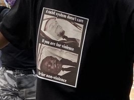 у негры на футболке надпись "Расистской системе все равно. Если вы за насилие. Или за ненасилие." (мёртвые Малколм Экс и Флойд)