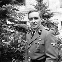 "На самом деле на такой машине в те времена ездили члены правительства, а трехбуквенных номеров не было." (с)
Да там много чего показанного в фильме на самом деле не было. Например черная форма офицеров СС и Гестапо, в которой ходил Щтирлиц, Мюллер и прочие, ко времени, показанном в фильме, а это конец войны 44-45 года, уже не существовала. Ее не существовало уже к 39 году. В фильме есть кадры, где Штирлиц в "правильной" для того времени форме СС. Но слышал такую версию, что режиссер Лиознова тоже знала об этом моменте с формой, но выбрала все равно черную, старую форму СС, она выглядела зловеще)).
Вот исторически правильная форма офицеров СС того времени: серо-голубоватый китель и такие же брюки. Это кадр не вошедший в фильм: