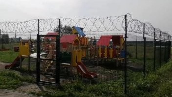 если район такой, что простой забор не помогает - и местное быдло ломает площадку - то колючка по верху себя оправдывает.

правда вызывает вопрос расположение площадки - судя по фото, которые нашлись в сети она стоит не "во дворе" а на краю жилого района - и дальше начинается промзона ...