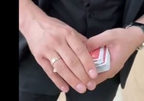 На 16 секунде выбирается карта, на 17 секунде видно как она мелькает под обручалкой. 
Главное ее сразу вытащить и положить или в начало или в конец, а дальше манипуляции просто для красоты.