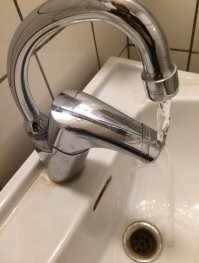 Это не дизайнер накосячил, а тот кто кран ставил.  У меня стоит такой, но в углу раковины: корпус параллельно стене,  а кран 45градусов льет в центр раковины.