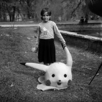 Работа фотографа Александра Чекменёва. Детский аниматор в парке культуры имени Первого Мая, выпивает после рабочего дня (Луганск середина 90-х).

Источник:  © Fishki.net
Это действительно снимок, сделанный Александром Чекменёвым в Луганске, но не в середине 90-х, в 2003. Сам Пикачу-то только в 1996 появился.
На самом деле это целая серия фотографий с интересным продолжением. Вот что рассказывает про эти снимки сам автор: 
"Это Луганск. Парк культуры и отдыха имени Первого мая. Там встретил знакомого фотографа, с ним товарищ в костюме Покемона   дети с ним фотографировались. Уже вечер, решили выпить коньячку. Разлили по пластиковым колбочкам из-под фотоплёнки, этот товарищ только голову снял, и тут девочка подошла   попросила с Покемоном её снять. Взяла эту голову и надела на себя. Мы это увидели и замолчали   какой-то особенный, печальный был момент."
И спустя 18 лет после того как были сделаны фотографии Чекменёв решил разыскать ту самую девочку:
"Известный украинский фотограф, автор книги “Donbass” Александр Чекменёв объявил в соцсетях о поиске героини своего снимка "Покемон". Он ищет девочку, которая сфотографировалась 18 лет назад в Парке 1 мая Луганска, но так и не забрала фото.
Фотограф разместил объявления о поиске в соцсетях, где рассказал историю снимка.
“Эта история произошла со мной в 2003 году в Луганске, откуда я родом. В Парке 1-го Мая я встретил друзей-фотографов, один из которых отработал свой съёмочный день в одежде сказочного персонажа. Решили, что больше съёмок не будет, и взяли бутылочку, на туловище чудо-персонажа поставили пластмассовые стаканчики и налили по первой”,   рассказывает Александр.
Тем временем, к фотографам подошла девочка и попросила сфотографироваться с мультяшным персонажем."