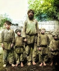 Особенно доставляет крестьянин на заднем плане - в шляпе, костюме-тройке и при галстуке. 
Судя по найденной информации, фотография из коллекции некоего А.В.Живаго (доктор, член Русского фотографического общества), 1897 год . 
Семья, запечатлённая на фото, явно не простая крестьянская. Справный дом под железной крышей, водостоки, кирпичный фундамент, большие застеклённые окна с кружевными занавесями, резьба и витые столбики, мальчик в сапожках по размеру... 
Видимо, сельские богатеи, кулаки. 
Сравните с настоящей крестьянской семьёй и с типичным деревенской избой, объединяющей под одной крышей жилую зону и хлев с конюшней.