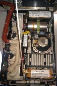 Boeing-737 NG
В верхней и нижней (по фото) частях PSU находятся отсеки кислородных масок пассажиров.
Кислород в маски поступает по серому шлангу, виден с правой стороны.

Кислород к ним поступает из химических генераторов. Металлический цилиндр на фото. Это и есть Oxygen generator. По одному такому генератору приходится на каждый двойной или тройной блок кресел.

Генератор вырабатывает кислород в результате химической реакции хлората натрия с железом, и остановить его невозможно.
Длительность его работы порядка 15 минут. Во время работы генератор нагревается до температуры порядка 230 градусов. Оранжевая полоска на корпусе генератора чернеет при нагреве и показывает, что генератор использован.

В левой части генератора видно устройство его запуска.

Принцип тут примерно как у ручной гранаты - есть подпружиненый боёк, который удерживается небольшим штырём.
Как только штырь вытащен, боёк ударяет в запал и таким образом инициирует химическую реакцию.
Штырь вытаскивается только чисто механически, никакого электропривода нету.
Тросик от штыря через систему колёсиков соединяется с верёвочками, на которых повисают вывалившиеся кислородные маски: