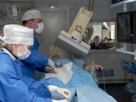 Так, ну то чтоб от ликвидатора ЧАЭС защищаться фартуком, понятно лютый бред, даже если б там (в Чернобыле) был настоящий атомный взрыв и сопутствующий нейтронный поток давал бы наведённую радиоактивность на окружающие предметы, то человека он бы радиоактивным не сделал бы таким образом.. не тот материал, чтоб иметь такие свойства. Точнее сделал бы. но это была бы "смерть под лучом" и фонящая лужа биомассы (как при взрыве в б. Чажма)
Человек может нахватать на себя радиоактивной пылищи и грязи, после чего будет опасен как для самого себя, так и для окружающих - но я думаю к 1990 году, уже все ликвидаторы ЧАЭС догадались помыться и постричься.. а кто не догадался (гипотетически), то уже бы помёр от лучевой. Да и даже если мы представим, что не помер - то защищаться от не не фартуком надо, а обычной одноразовой одеждой, перчатками и марлевой повязкой, чтоб самому не нахвататься и не надышаться  радиоактивной пыли.
Это я так, в сторону ушёл. Автор наверное скопировал с иностранного и перевёл в силу скудоумия, через какой-нить гугл переводчик подписи, после чего не перечитывая - запостил сюда.
Предположу, что операция действительно делалась ликвидатору ЧАЭС, но  врач в фартуке по другой причине. Есть ряд оперативных вмешательств, когда на счету каждая минута, и требуется прям вот на операционном столе сделать снимок (или череду снимков) для чего там работает рентгеновская установка, а врачи - находятся в специальных фартуках. Больному помощь нужна, а им лишние мегаэлектронвольты совсем не нужны. 
Такое моё предположение. Делались ли подобные операции в 1990 году, я не знаю. Впрочем я и не могу гарантировать что на фотке хирург, а не работник рентген кабинета. Такие вот дела.