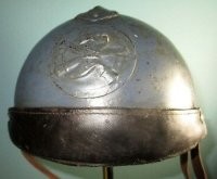 Это каска Адриана 1915 года M15, символ в виде скрещенных пушек указывает на артиллерию. Существовала каска Адриана с защитной маской Поллака



Маска в посте скорее всего окопный колхозинг.



У модификации каски для экипажей бронетехники M19 спереди отсутствовал козырёк, вместо которого имелся кожаный амортизатор. Гребень был на 40 мм короче, чтобы оставалось место для размещения эмблемы.