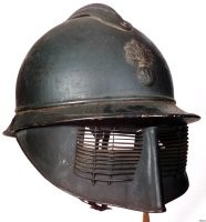 Это каска Адриана 1915 года M15, символ в виде скрещенных пушек указывает на артиллерию. Существовала каска Адриана с защитной маской Поллака



Маска в посте скорее всего окопный колхозинг.



У модификации каски для экипажей бронетехники M19 спереди отсутствовал козырёк, вместо которого имелся кожаный амортизатор. Гребень был на 40 мм короче, чтобы оставалось место для размещения эмблемы.