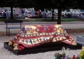 Может показаться, что могила знаменитого танцора Рудольфа Нуриева во Франции укрыта настоящим старинным ковром. Многие туристы даже спрашивают – не вредит ли ковру дождь… Дождь ему не страшен – ведь надгробие сделано из камня и украшено тончайшей мозаикой.
В 1996 году надгробие было изготовлено в итальянской мозаичной мастерской Акомена Спацио Мозаико (Akomena Spacio Mosaico). Мозаика ковра выполнена из мелких преимущественно квадратной формы элементов с плотнейшим прилеганием деталей, практически без видимых швов. Но при этом поверхность мозаики оставлена шероховатой, с весьма резкими изменениями уровня мозаичных элементов. Этот прием с расстояния уже 2-3 метров создает общее впечатление ковровой текстуры.