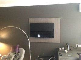 Более чем уверен, что телевизор на кронштейне и просто немного повернут к кровати. Нажать на правый край и прижмется к стене по центру.