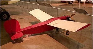 "В 1946 году Мортенсон работала сборщицей дронов на авиационной фабрике"
Таки да, именно дронов.
Работала она на фирме Radioplane Co. Inc., которая во время войны выпускала самолеты и самолётики, управляемые по радио.
К фото ниже:
Role	    Target drone
National origin	United States
Manufacturer	Radioplane
First flight	1939
Primary user	USAAF
Number built	ca. 15,000
Ну, а на второй фотографии - сама героиня с пропеллером в руках.
