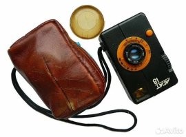 У того же "Агата" объектив если и выступал, то сантиметр где-то и поставлялся он как раз с сумкой, как на фото. А в более позднем Агат 18К и от сумки отказались, он уже шёл просто с крышечкой на объектив. Вполне себе советская мыльница, ещё и полуформатка, 72 кадра на стандартную плёнку. 
А уж если складни вспомнить, у которых объектив убирался в корпус, так они с ещё раньше были. Та же "Искра" например. Правда они шли с обычными в те времена кожаными кофрами, хотя и плоскими.