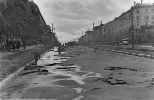 Снимок №5 "Потоп на пл.Труда" из серии снимков 1959 года сделаных жителем Восточного посёлка (это адрес такой) Георгием Викторовичем Жаннин-Перро. Он вообще много снимал Новосибирск и вот часть этой серии. В тот летний день с юго-востока пришла чёрная, налившаяся над Обью, избытком воды, она сначала обрушила водяной шквал на строящийся район "Башня", а потом накрыла Первый соцгород, где все переулки и улицы были мощёны булыжником, а центральную улицу Станиславского упиравшуюся в только, что построенный и открытый новый путепровод под Транссибом, свеже заасфальтированную для пуска троллейбусного движения к заводам.  Ливнёвка на площади Труда в мгновение ока была забита обломками смытого асфальта и площадь превратилась в озеро. Но кому проблемы, а детям и тут игра - вода-то пришла тёплая, нагретая взломанным дорожным покрытием. И вот благодаря Георгию Викторовичу, мы можем увидеть результат работы того ливня.