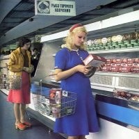 По многим признакам. Скажем так, это на похоже на спонтанную фотографию, вроде того, что кто-то случайно зашёл в магазин и сфотографировал. Тут видна композиция кадра. Чёткий ракурс перспективы, для чего снимок был сделан с использованием вышки или штатива на высоте 3-3,5 метра. Для обычной работы магазина в кадре очень малолюдно. На переднем плане стоят женщины, изображающие покупательниц. Они без сумок, корзинок и тележек в картинной позе стоят у прилавка и старательно изучают консервную банку в руках. Расстояние между ними строго выверенное, чтобы эти пять человек максимально заполняли собой пространство. При этом кроме них в зале магазина нет вообще никого, хотя пространство в кадре просматривается огромное. На заднем плане пусто. 
Вообще, это характерно для печатной продукции тех лет. Если посмотреть другие фотографии из этого сборника, то там всё то же самое. На них никаких очередей, полки заполненные товаром и улыбающиеся нарядные женщины как с рекламного проспекта. Впервые живые непостановочные фотографии в СССР стали массово публиковать в журнале "Смена" начиная с 1989 года. Это придало журналу изрядную популярность. Потому что разница живых фото с этими глянцевыми советскими картинками была разительной.