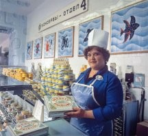 По многим признакам. Скажем так, это на похоже на спонтанную фотографию, вроде того, что кто-то случайно зашёл в магазин и сфотографировал. Тут видна композиция кадра. Чёткий ракурс перспективы, для чего снимок был сделан с использованием вышки или штатива на высоте 3-3,5 метра. Для обычной работы магазина в кадре очень малолюдно. На переднем плане стоят женщины, изображающие покупательниц. Они без сумок, корзинок и тележек в картинной позе стоят у прилавка и старательно изучают консервную банку в руках. Расстояние между ними строго выверенное, чтобы эти пять человек максимально заполняли собой пространство. При этом кроме них в зале магазина нет вообще никого, хотя пространство в кадре просматривается огромное. На заднем плане пусто. 
Вообще, это характерно для печатной продукции тех лет. Если посмотреть другие фотографии из этого сборника, то там всё то же самое. На них никаких очередей, полки заполненные товаром и улыбающиеся нарядные женщины как с рекламного проспекта. Впервые живые непостановочные фотографии в СССР стали массово публиковать в журнале "Смена" начиная с 1989 года. Это придало журналу изрядную популярность. Потому что разница живых фото с этими глянцевыми советскими картинками была разительной.