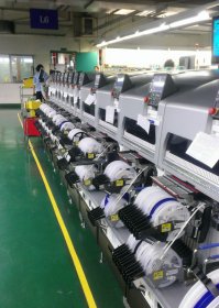 Там фотография всего цеха была и если эта тётушка паяет образец, то кроме образцов тот цех ничего не выпускает. Отличие фоток с Gigabyte достаточно очевидно - во-первых там конвейер. Во-вторых те, кто занят ручным трудом, расставляют на плату крупные компоненты, поставляемые  россыпью. С SMD к этому моменту уже закончили, а выглядело это как на картинке ниже (картинка с того же завода). Катушки, подвешенные снаружи автоматов, как раз содержат ленты с SMD.
Причём Gigabyte это ещё не самое технологичное производство - там, например, контроль осуществляется визуально, в то время как на большинстве других заводов изображение платы с установленными компонентами анализирует компьютер.